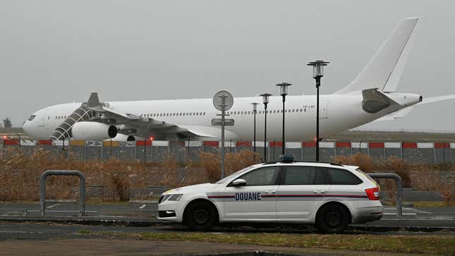 This photograph taken on December 25, 2023, shows a French customs car with an Airbus A340 in the background which was grounded on the tarmac since December 21 over suspected "human trafficking", at the Vatry airport, north-eastern France